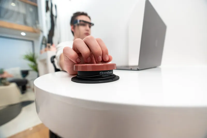 Person using GlassOuse press switch assistive device with laptop for environmental control